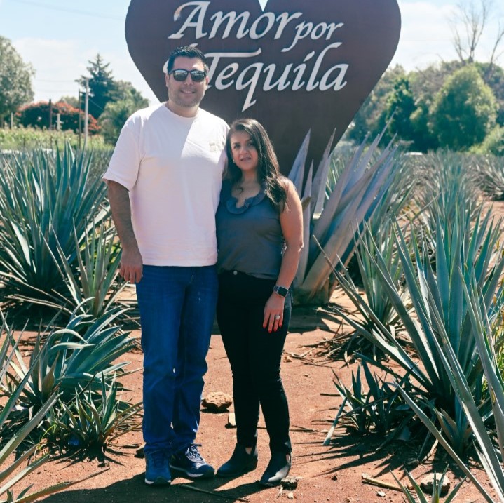 Roberto Leon and guest in a blue agave field in front of the Amor por Tequila sign in Jalisco